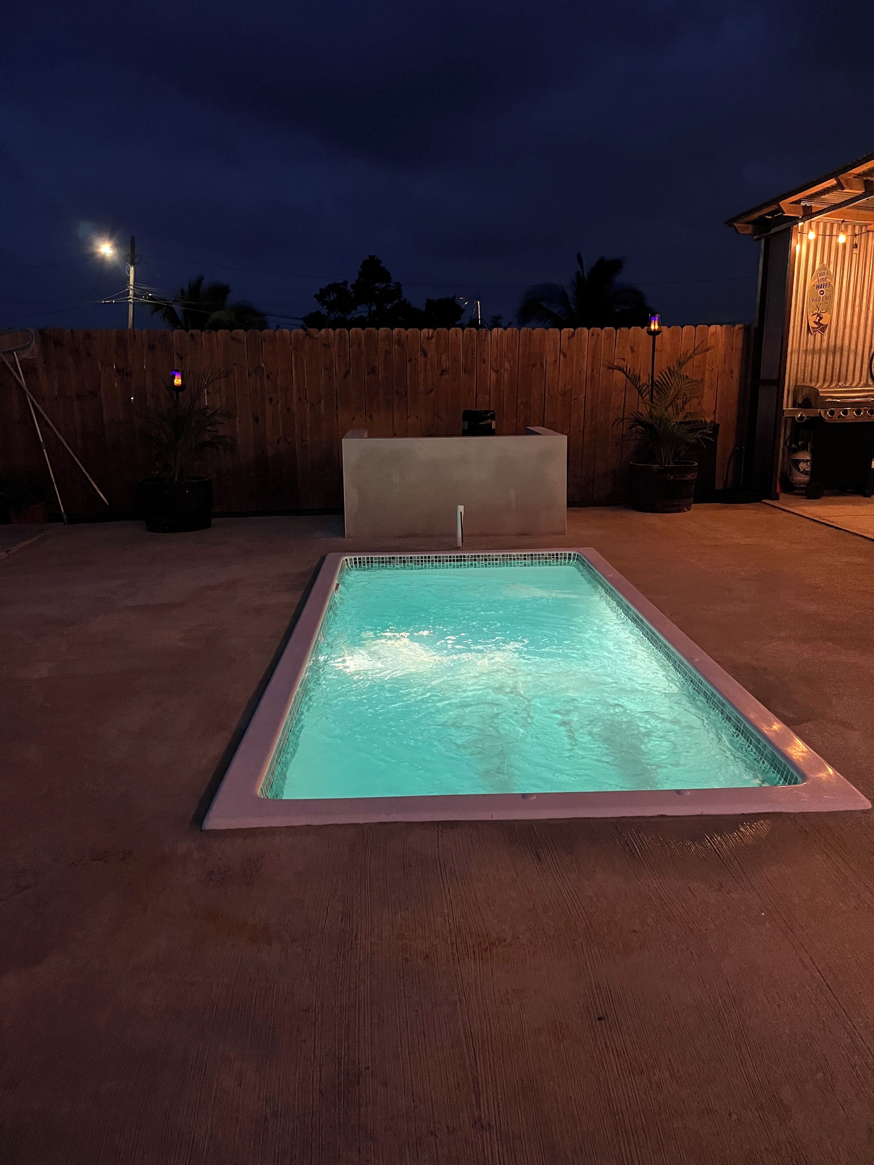 A rectangular swimming pool with a tiled edge, surrounded by a wooden deck and a wooden fence.