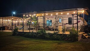 A well-lit RV with a covered porch and string lights, surrounded by a grassy area. - El Camper with private pool (Maleza Alta)