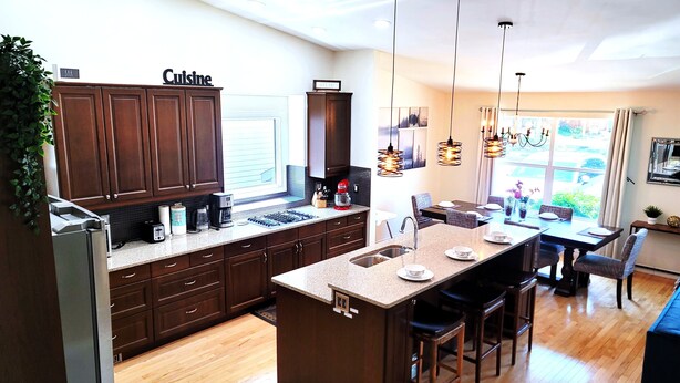A modern kitchen with dark wood cabinets, a central island with bar stools, and a dining area with a view of the outdoors.