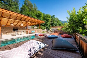 Eine Holzterrasse mit Pool, Sitzgelegenheiten im Freien und einem überdachten Bereich mit einer Steinmauer.