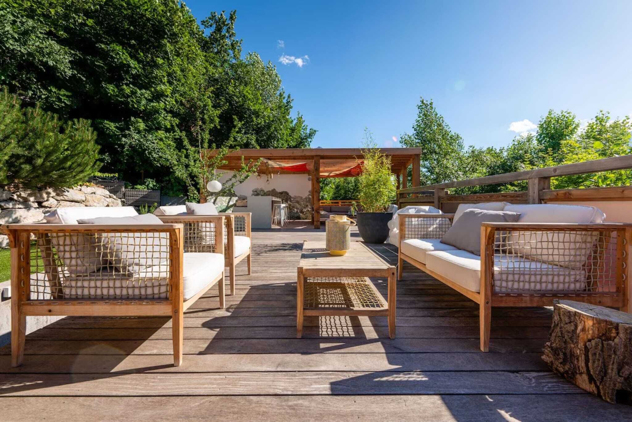 Une terrasse extérieure aménagée avec du mobilier en bois, comprenant des canapés et des fauteuils, une table basse et une structure en forme de pergola.