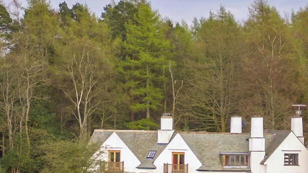 Une rangée de maisons blanches aux toits gris, entourées d’arbres denses.