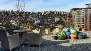 Un espace patio aménagé avec des meubles en osier, des plantes en pot et un mur en pierre.