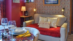 Une pièce chaleureuse avec un canapé, une table à manger avec des assiettes et des verres, une lampe et un tableau encadré au mur.