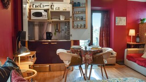 Un espace de vie compact comprenant un coin cuisine, un coin repas avec une table et des chaises, un canapé et un lit recouvert d’une couvre-lit à motifs floraux.