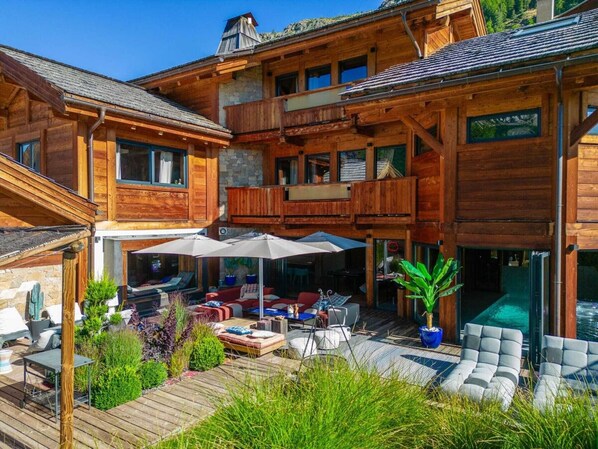 Un bâtiment en bois à plusieurs étages, doté d’un espace extérieur couvert avec des sièges, d’une piscine et d’une façade en pierre.