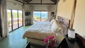 Une chambre avec un grand lit, un hamac et une vue sur l’océan.