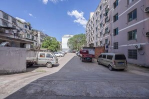 Eine schmale Stadtstraße mit geparkten Fahrzeugen, mehrstöckigen Gebäuden und blauem Himmel.