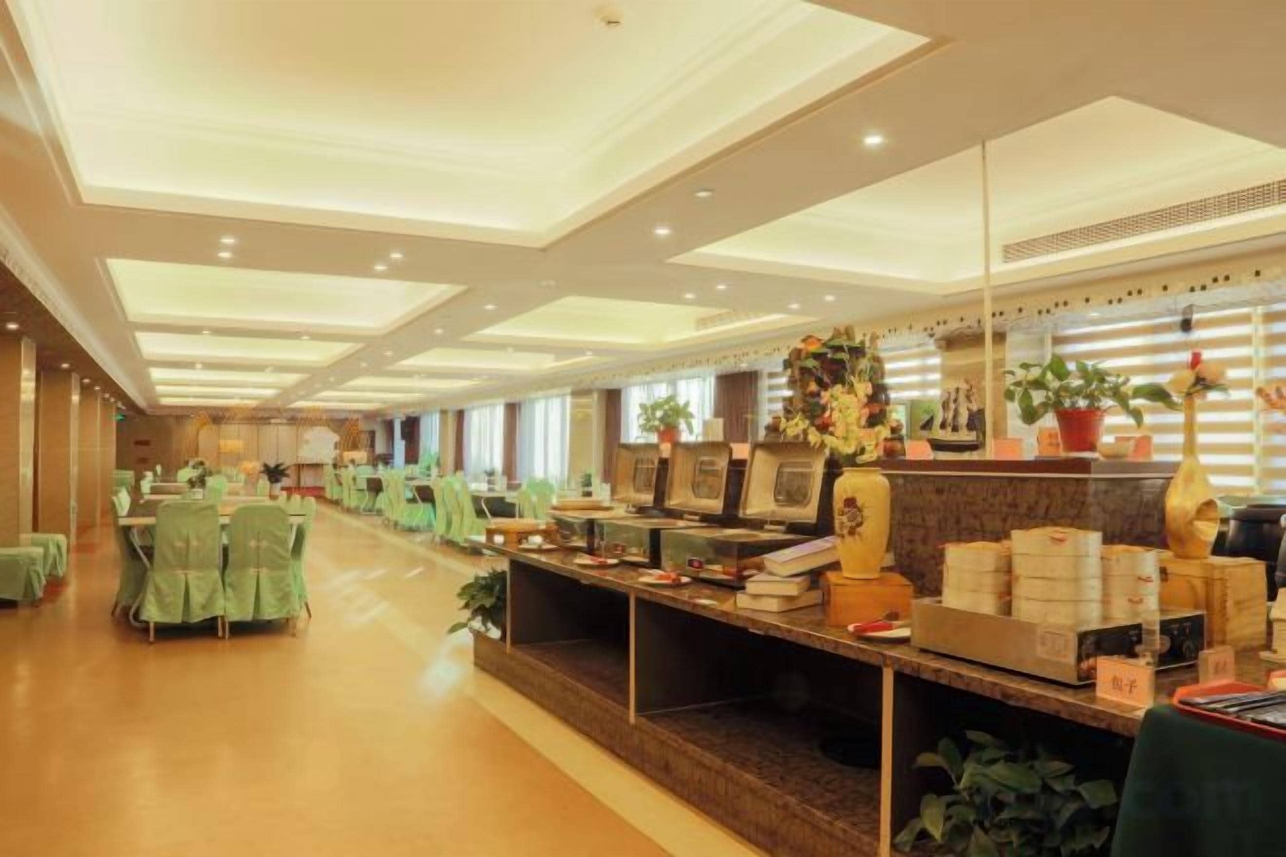 A hotel lobby with a long reception desk, green chairs, and potted plants.