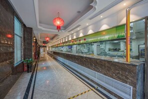 Een hotel lobby met een marmeren receptiebalie, rode lantaarns en een groene muur met sterren.
