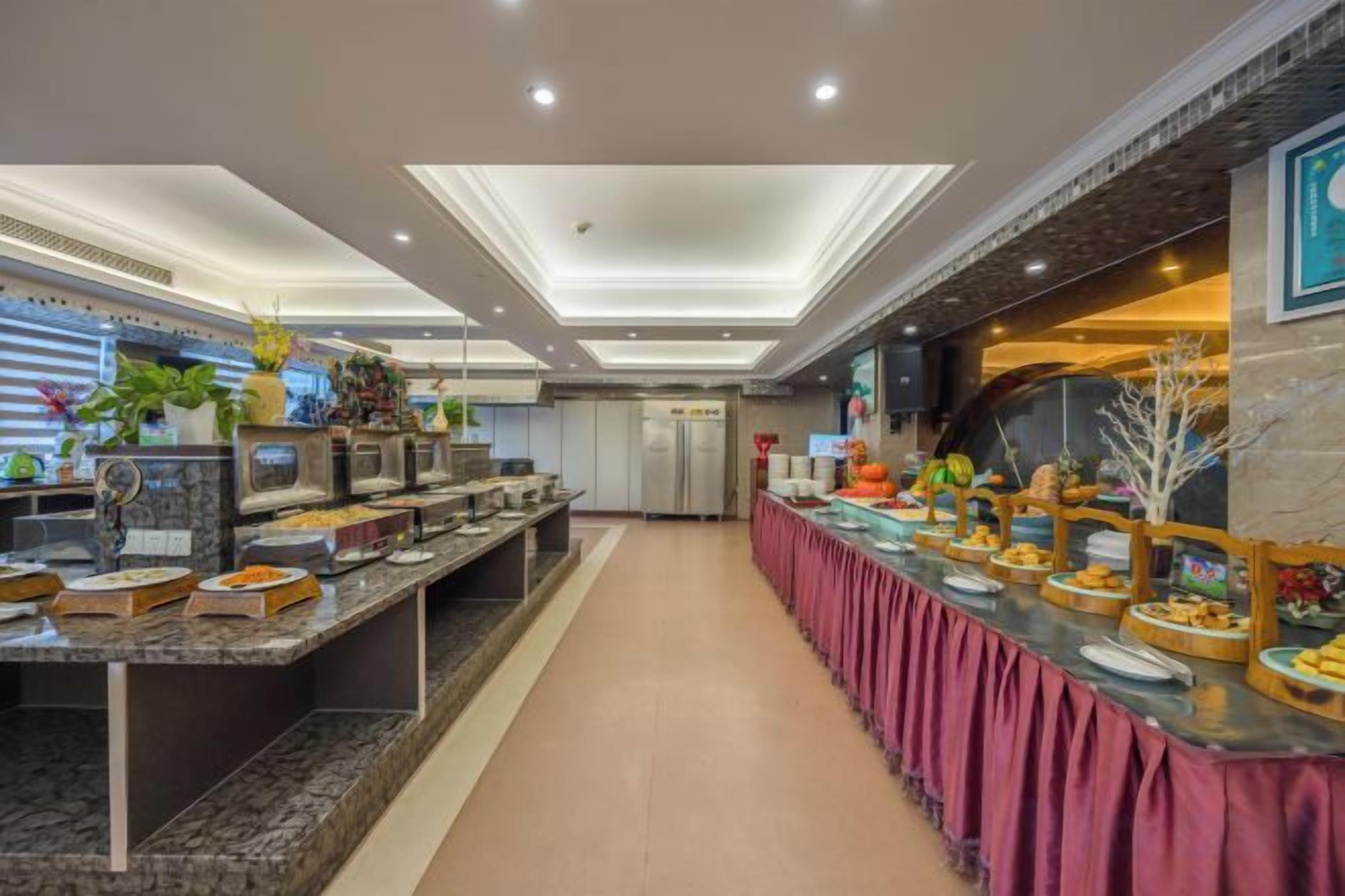 Un buffet avec plusieurs présentoirs de nourriture, un long comptoir recouvert d’une nappe rose et un décor intérieur moderne.