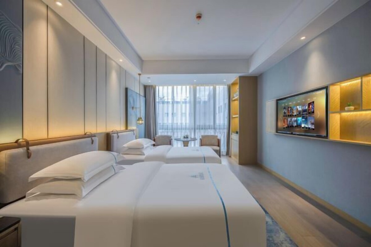 Une chambre d’hôtel avec deux lits, une télévision, une petite table et une grande fenêtre.