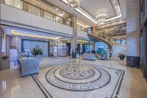 Eine geräumige Lobby mit Marmorboden, einer Rezeption, einer Treppe und einer großen Kronleuchter.