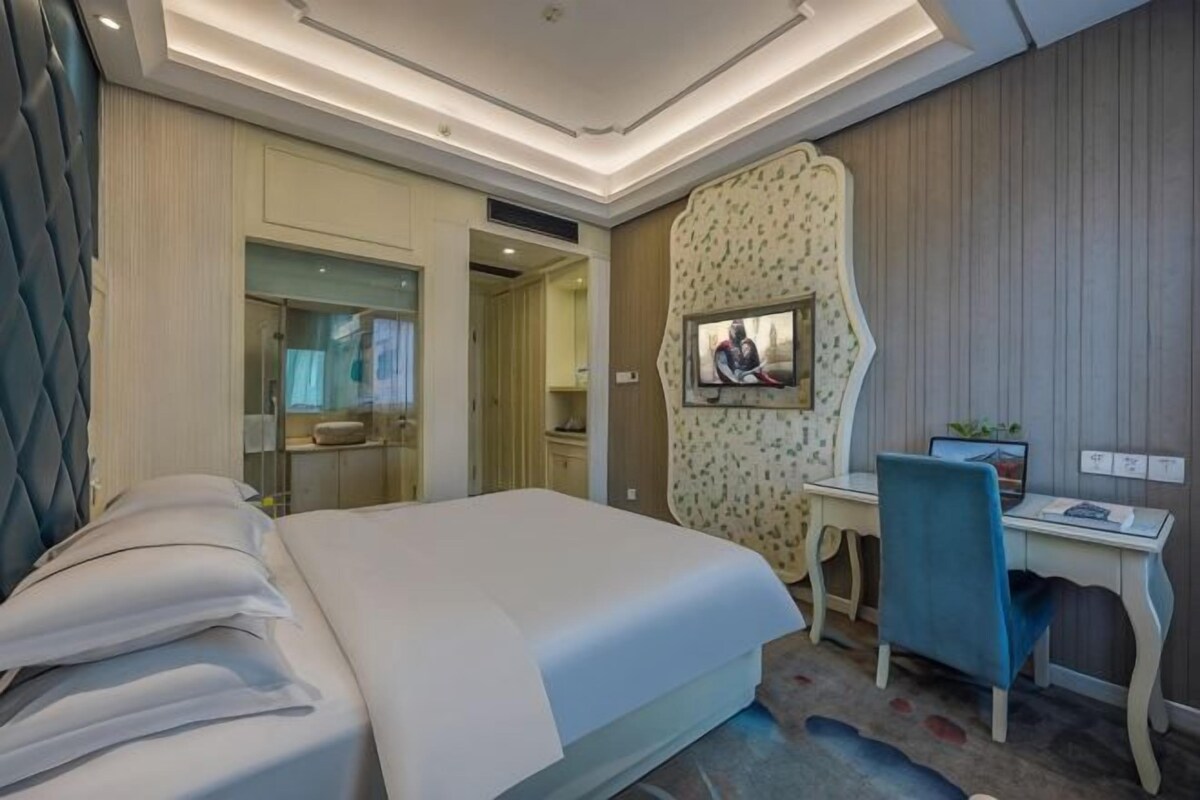 A hotel room with a bed, desk, chair, and a mirror.