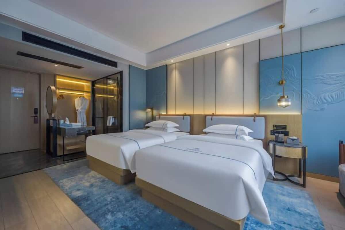 Una habitación de hotel moderna con dos camas, un baño con espejo y una pared de acento azul.