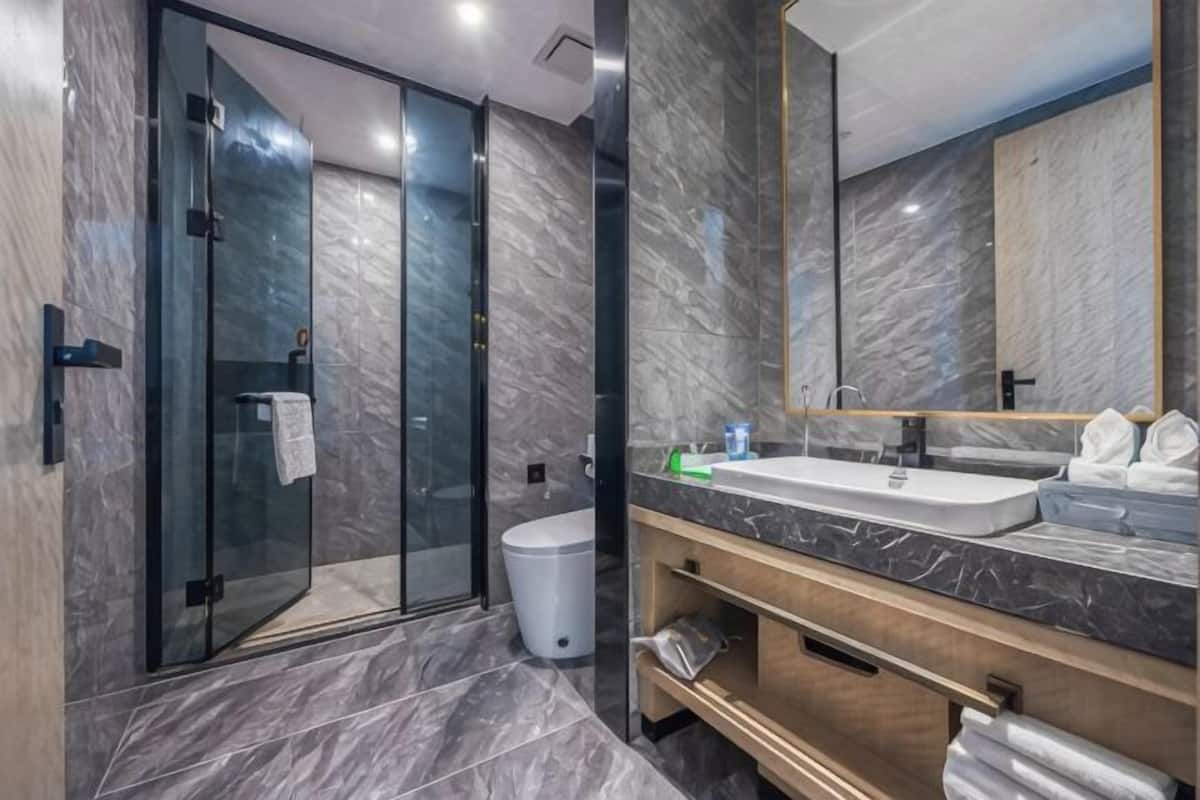 Un baño moderno con cabina de ducha de vidrio, suelo de mármol, un espejo grande y un mueble de tocador de madera.