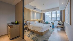 A modern hotel room with a large bed, a desk, a chair, and a balcony with a city view. - Wangfu International Hotel (Yiwu)