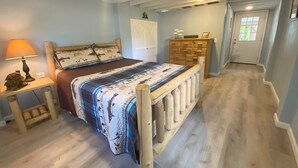 Una camera da letto con un letto in legno, un comodino con una lampada, un comò e una porta che dà su un'altra stanza.