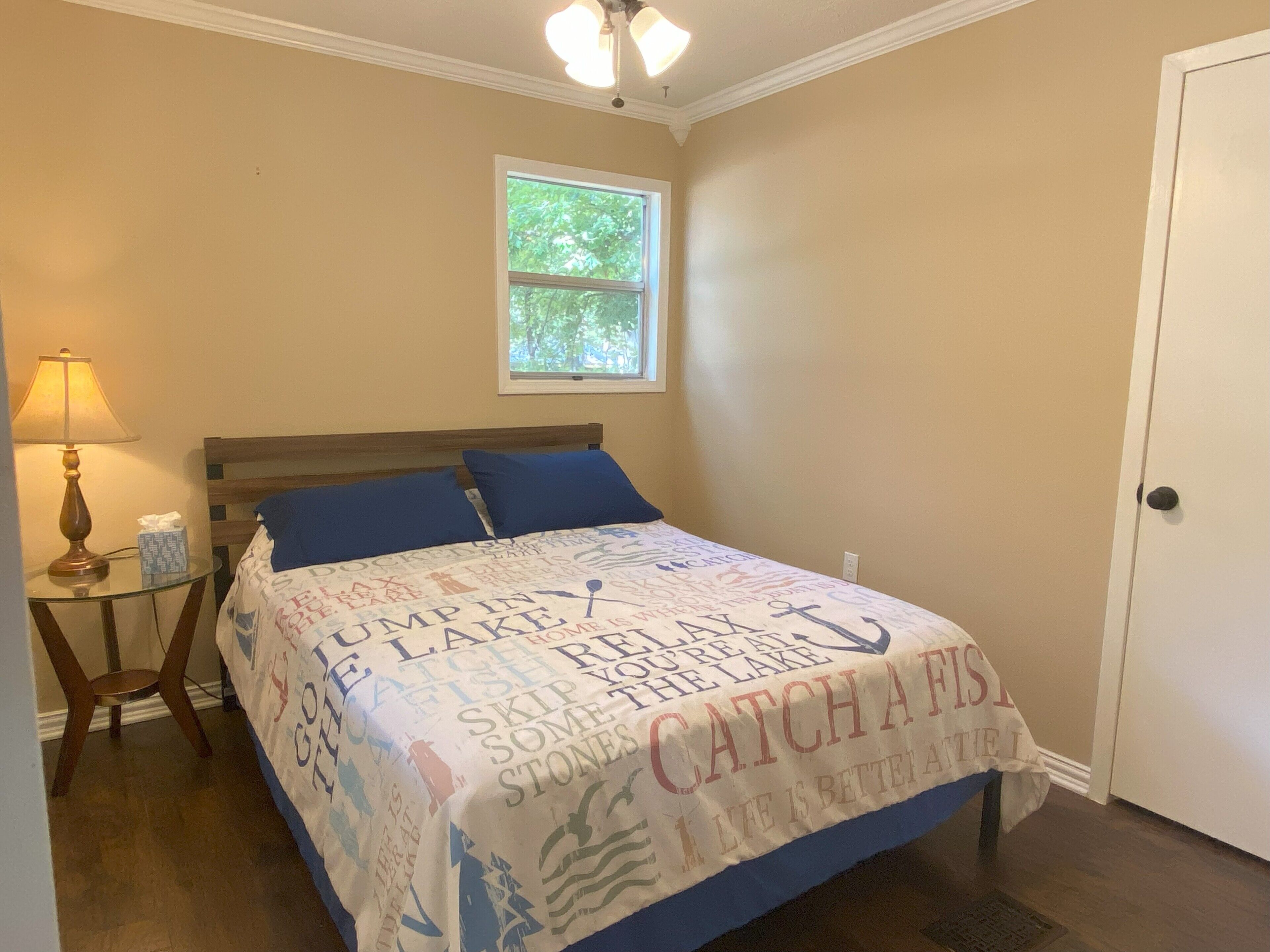 Une chambre à coucher avec un lit, une table de chevet, une lampe, une fenêtre et une porte.