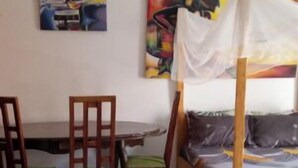 Una habitación con una cama, una mesa y sillas. Hay dos cuadros en la pared.
