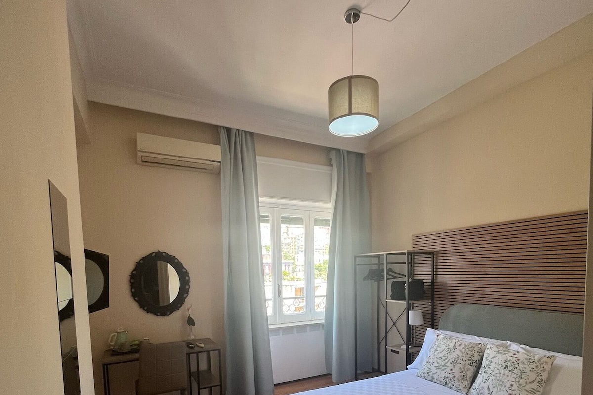 A bedroom with a bed, a desk, a chair, a mirror, and a window with curtains.