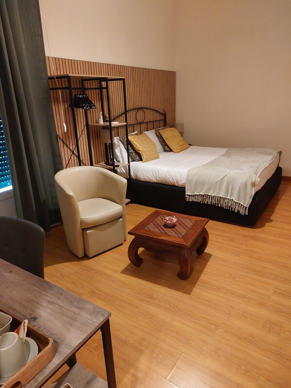 A hotel room with a bed, a chair, a small wooden table, and a window with curtains. - Domus Schipa (Naples)