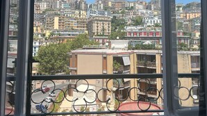 A view from a window with a metal balcony railing, overlooking a densely packed urban area with various buildings and a clear blue sky. - Domus Schipa (Naples)