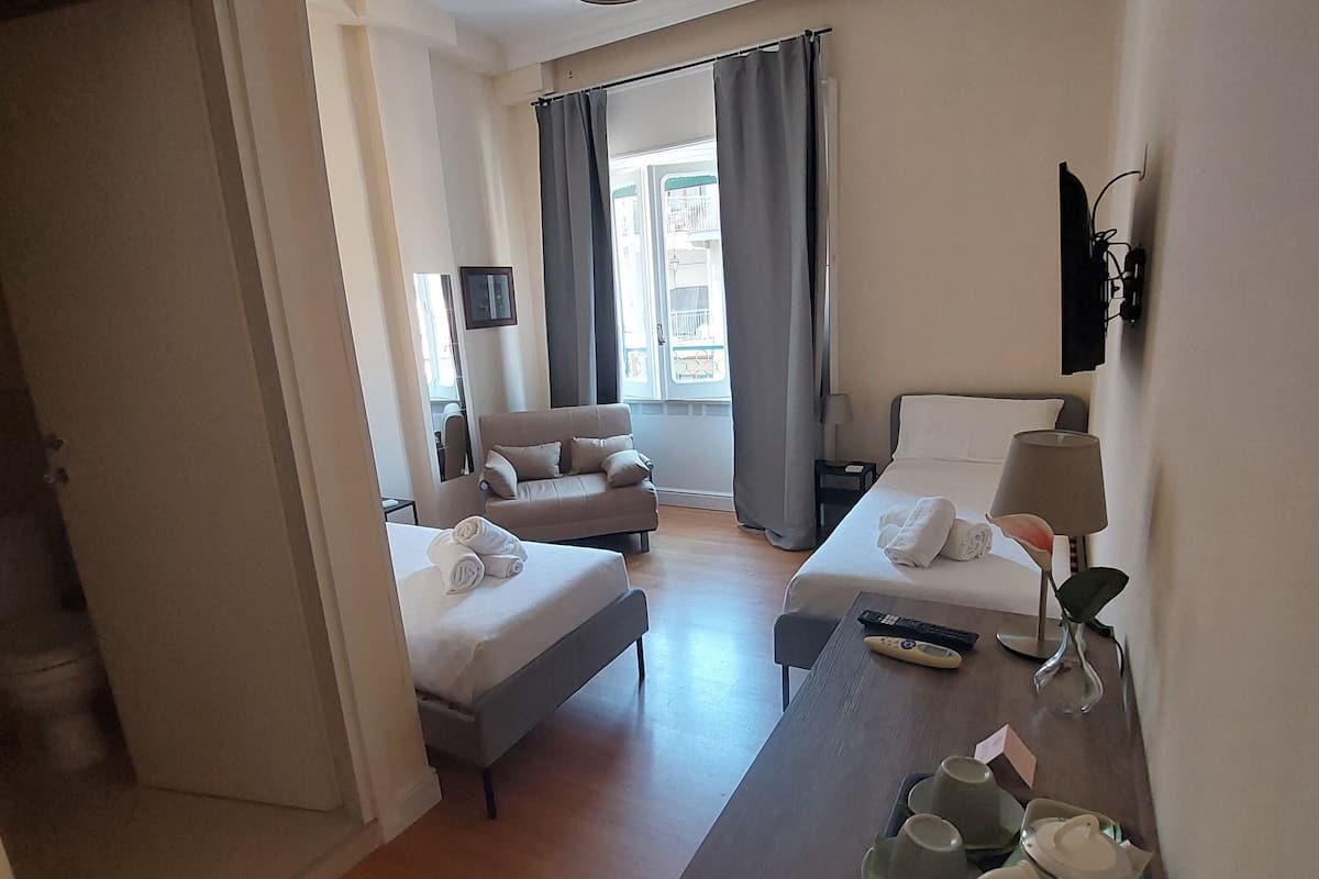 A hotel room with a bed, a sofa, a table with a lamp, and a view of the outside.