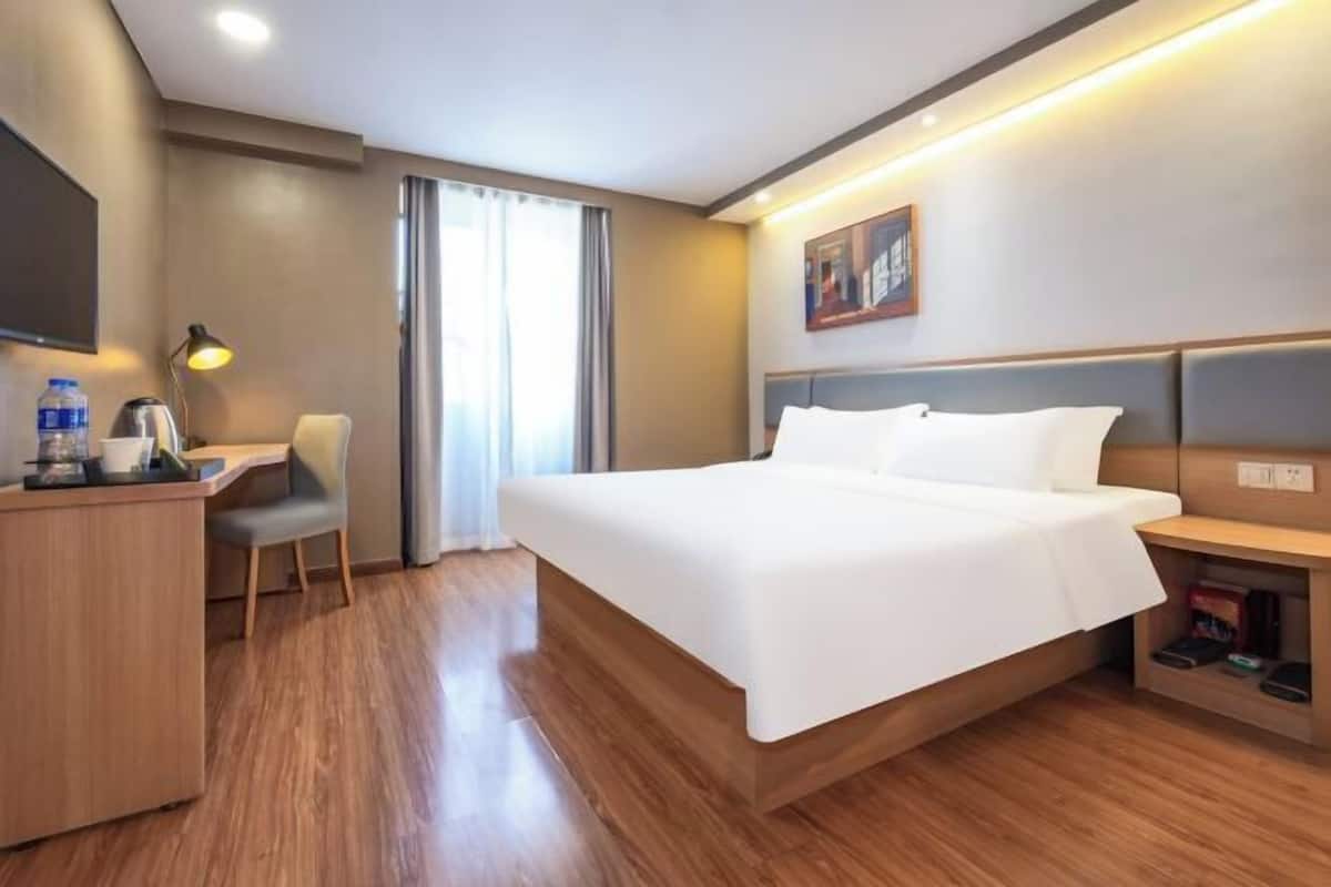 A hotel room with a bed, desk, chair, and a TV.