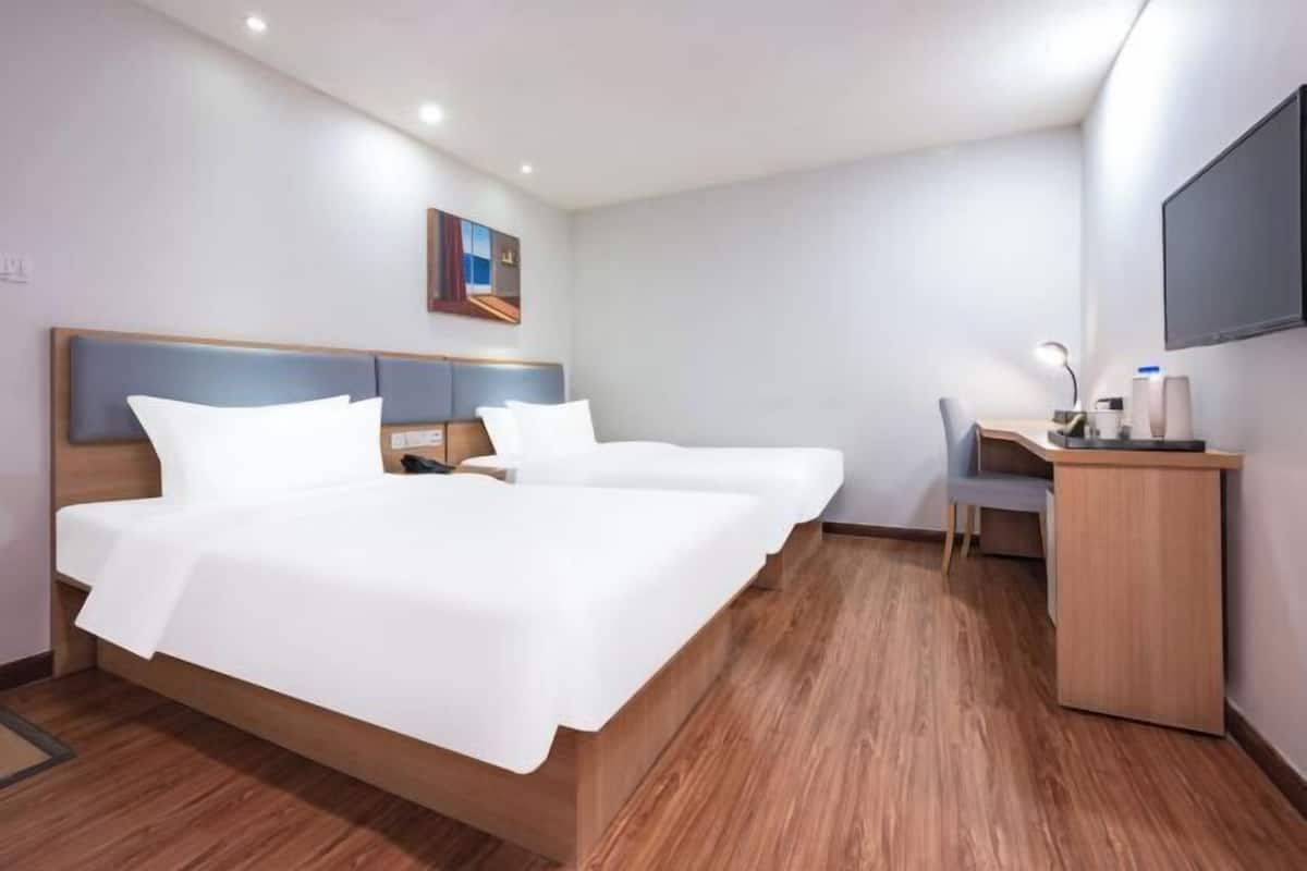 A hotel room with a large bed, a desk, a chair, and a TV on the wall.