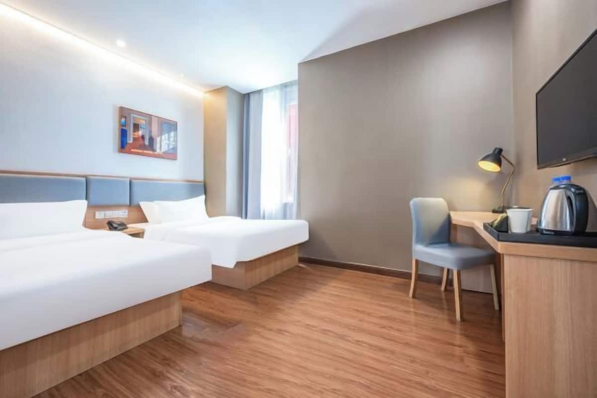 A hotel room with two beds, a desk with a chair, a flat-screen TV, a painting on the wall, and a window with curtains.