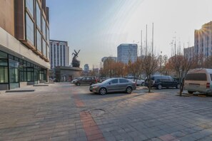 Une zone extérieure dallée, avec des voitures garées et un bâtiment doté de grandes fenêtres.