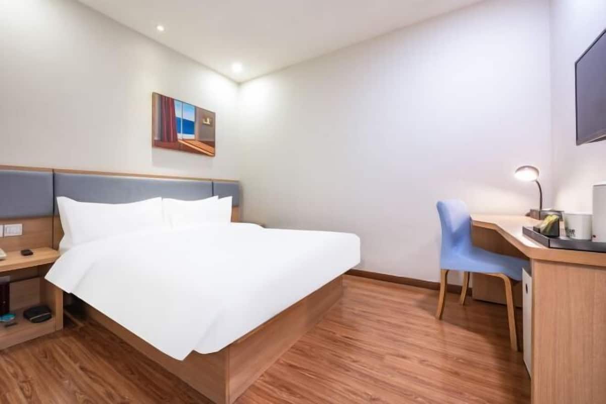 A hotel room with a bed, a desk, a chair, a desk lamp, and a painting on the wall.