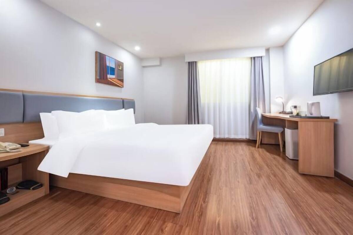 A hotel room with a bed, a desk, a chair, a television, and a window with curtains.