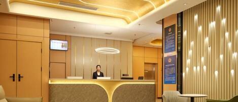A hotel reception area with a modern design, including a reception desk, seating area, and a television screen.