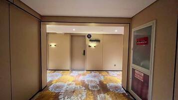A hotel corridor with a patterned carpet, a reception desk, and a sign indicating the location.