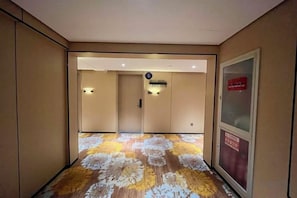 Pasillo de hotel con alfombra estampada, mostrador de recepción y un cartel que indica la ubicación.