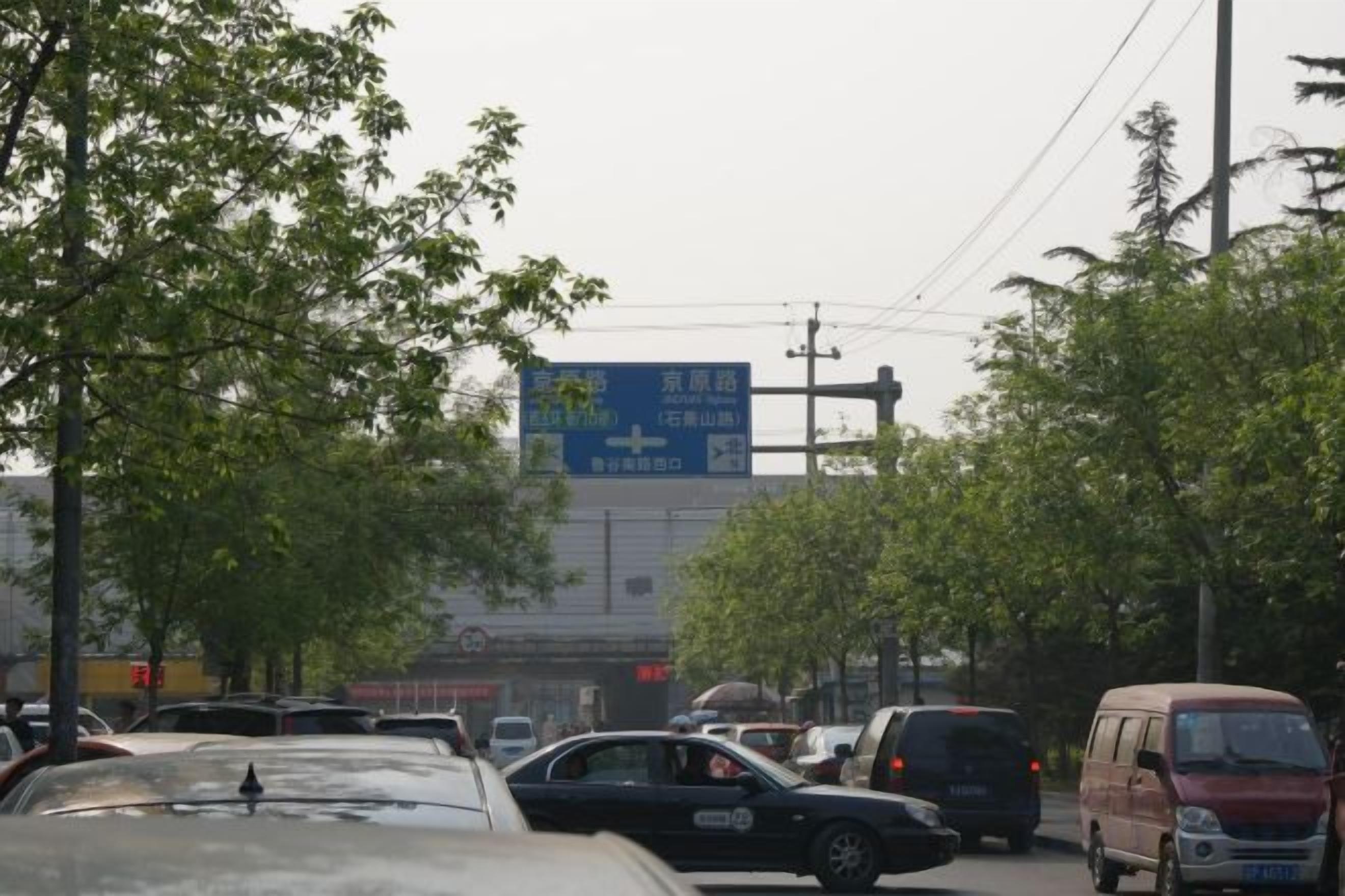 A busy street with multiple vehicles and a large blue sign in the background.