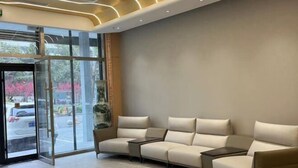 A modern lobby with a glass door entrance, a beige sectional sofa, and a small table. - Xin Maisui Hotel (Shijingshan Chaoyang Hospital West Campus) (Beijing)