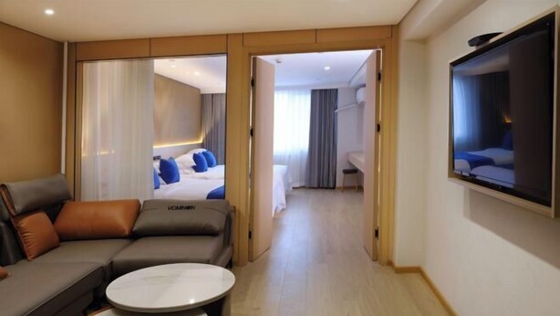 A modern hotel room with a sofa, a small table, a TV, and a bed with blue pillows. - Xin Maisui Hotel (Shijingshan Chaoyang Hospital West Campus) (Beijing)