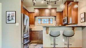 A kitchen with wooden cabinets, a stainless steel refrigerator, and a window with blinds. - Cozy Heights Hideaway :Pets welcome-Big Frontyard (Houston)