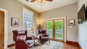 A spacious living room with two leather armchairs, a small table, and a floor lamp. There is a large window with a view of greenery and a sliding glass door leading to a balcony. - Cozy Heights Hideaway :Pets welcome-Big Frontyard (Houston)