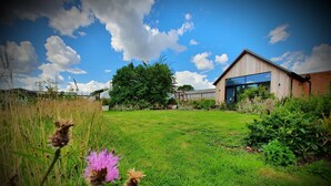 A modern building with a large glass window, surrounded by a well-maintained lawn and various plants. - The Flower Room - sleeps 2 guests  in 1 bedroom (Droitwich)