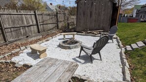 Ein Garten mit Feuerstelle, Holztisch und Adirondack-Stuhl.