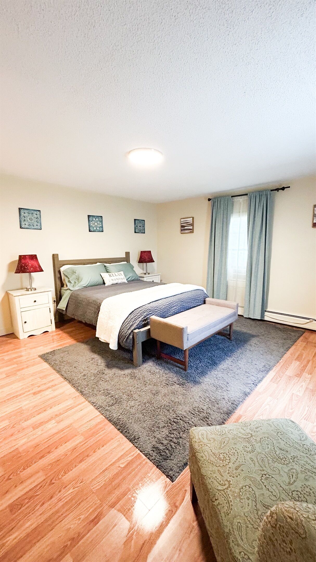 A bedroom with a bed, bedside tables, a bench, a rug, and a window with curtains.