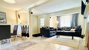 Ein geräumiges Wohnzimmer mit einer Couch, einem Couchtisch und einem Fernseher. Eine Tür führt in einen anderen Raum, und eine Lampe ist zu sehen.