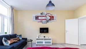 A modern bedroom with a sofa, a TV, a white cabinet, and a red blanket. - The Glowing Ruby | By Radiant Apartments (Wien)