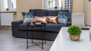 A modern living room with a grey sofa, patterned cushions, a small side table, and a potted plant. - The Glowing Ruby | By Radiant Apartments (Wien)