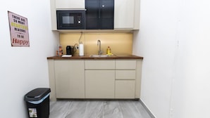 A small kitchenette with a microwave, sink, and cabinets. There is a trash bin and a motivational poster on the wall. - The Glowing Ruby | By Radiant Apartments (Wien)