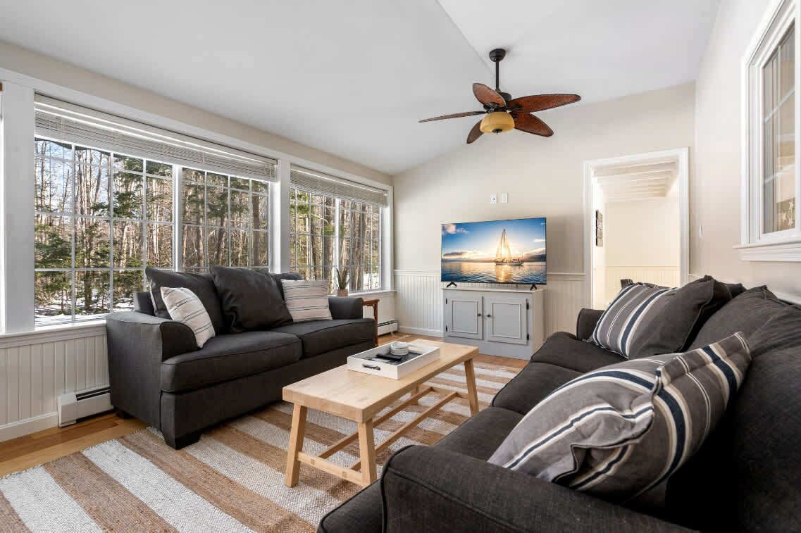 A modern living room with a large window, a ceiling fan, and a television.